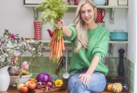 Megan Rossi sat on kitchen surface holding a bunch of carrots