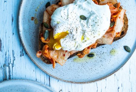 View Eggs are back on the menu! Two plates with one slice of toast kimchi and a poached egg with pumpkin seeds on top