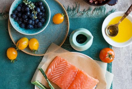 A spread of the Mediterranean diet showing a fillet of salmon, cavelo nero, tomatoes, blueberries, hazelnuts and olive oil