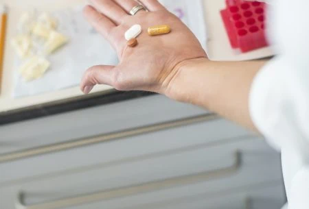 A hand showing 3 different types of pills