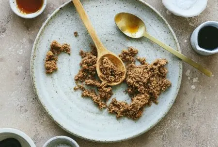 A plate of sugar, with two spoons and small bowls surrounding showing all different types of sugars and sweetners