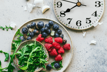 A plate of raspberries, blueberries and rocket alongside a traditional clock face showing the time of 8 o'clock