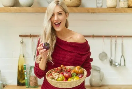 Dr Megan Rossi standing in kitchen holding a large bowl of mixed vegetables and smiling