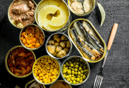 Bench top with large variety of canned foods on display, all with tops off to show food inside