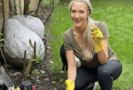 Dr Megan Rossi squatting down in garden outside, wearing gloves with one hand in the soil