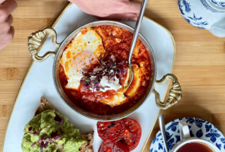 A table top with a savoury breakfast spread served on a long dish, and a china mug full of black tea to the side of the meal