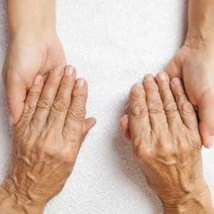 Two people holding hands, one pair of hands looks older than the other with more wrinkles