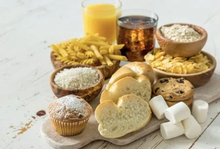 An image of carbohydrate containing foods, including: bread, pasta, cookies, a muffin, and two sugary drinks