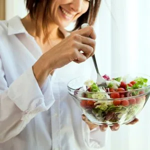 A photo of a woman eating a salad while smiling