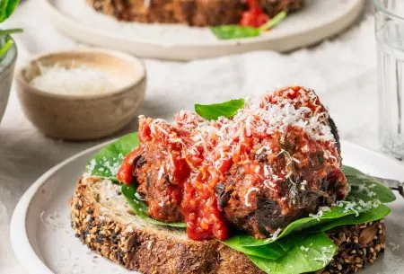 A photo of the meatless meatballs set on a plate. It's been served on top of sourdough bread, spinach and a sprinkling of cheese.