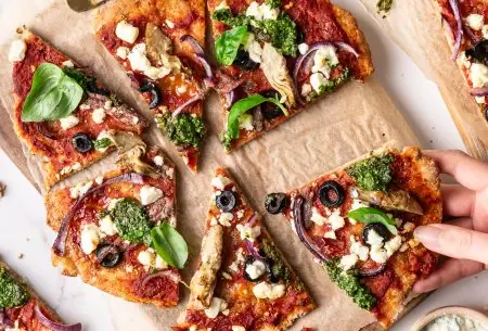 A photo of flatbread pizzas on a wooden board. One slice is being grabbed.