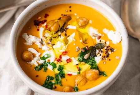 A photo of a bowl of pumpkin soup, topped with chickpeas, parsley & feta