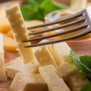 A photo of cubed cheese on a plate, with one being picked up by a fork