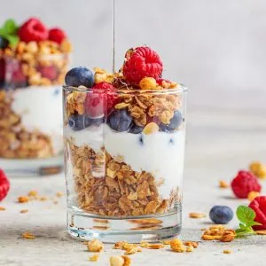 A photo of yoghurt, berries & granola in a glass cup