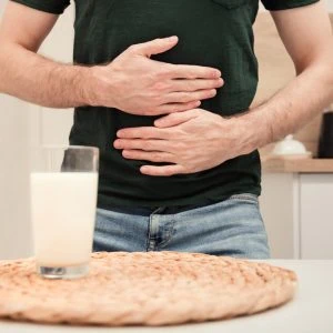 A photo of someone holding their belly with a glass of milk in front of them