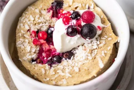 A photo of one of the mug cakes, in a white ramekin, topped with fresh berries and yoghurt