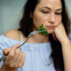 A photo of a woman holding a forkful of herbs