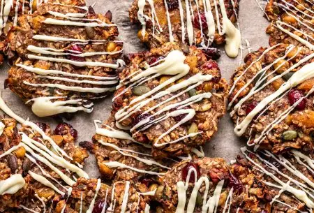 A photo of the trail mix cookies laid out on a table with white chocolate drizzled over them