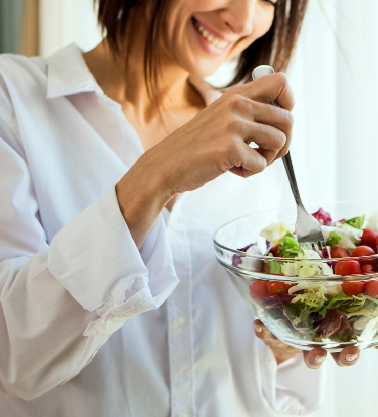 A photo of a woman eating a bowl of food while smiling