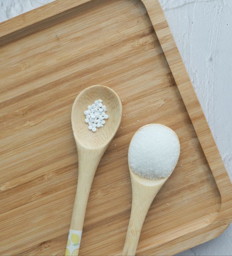 A photo of two wooden spoons, one with artificial sweetener and another with sugar