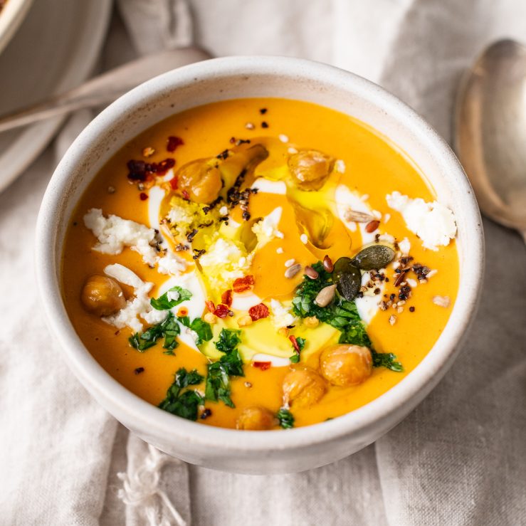 A photo of a bowl of pumpkin soup, topped with chickpeas, parsley & feta