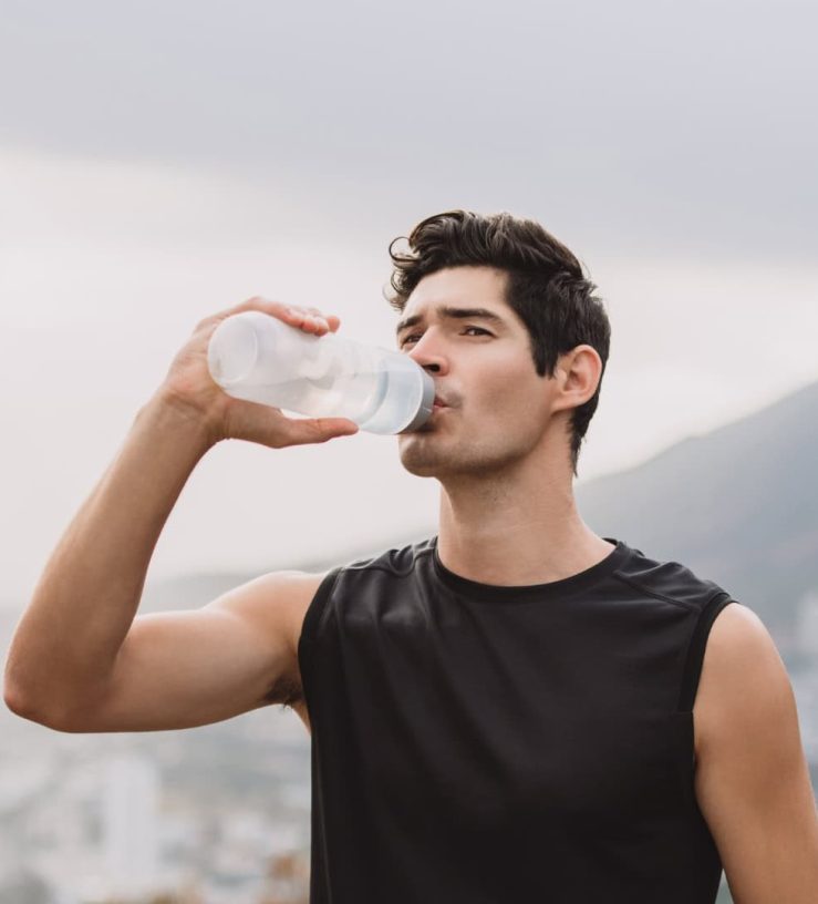 A photo of a man drinking from a water bottle in the middle of a hike