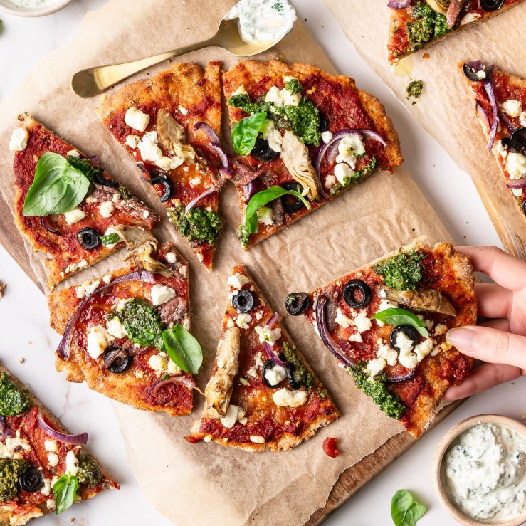 A photo of flatbread pizzas on a wooden board. One slice is being grabbed.