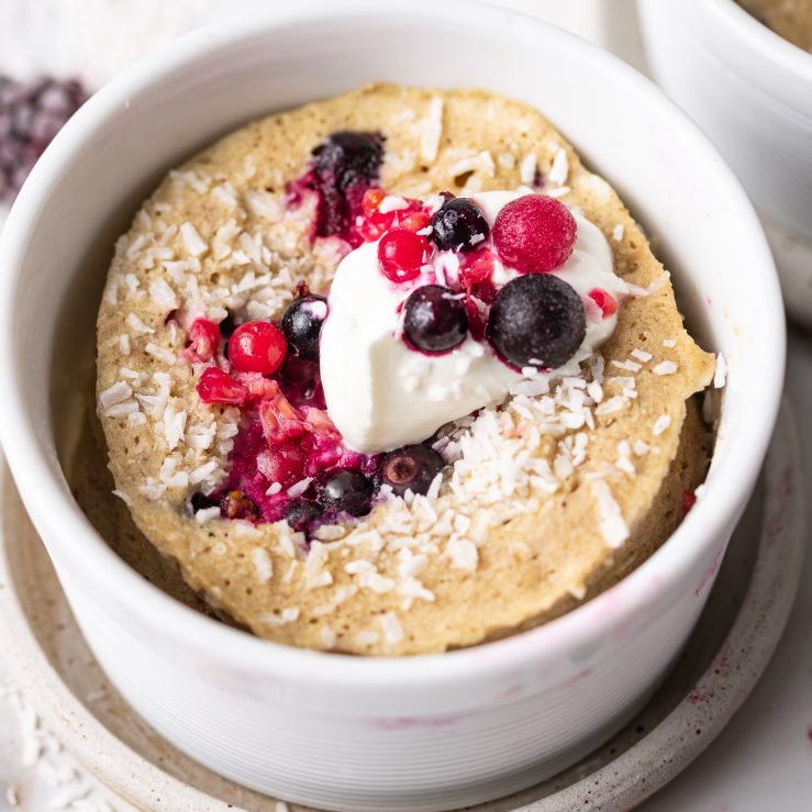 A photo of one of the mug cakes, in a white ramekin, topped with fresh berries and yoghurt