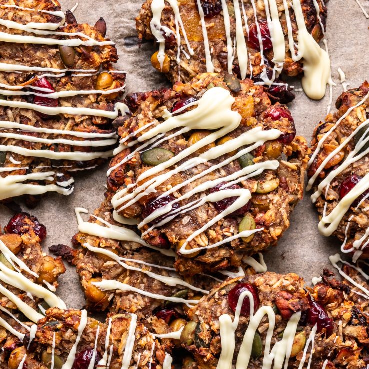 A photo of the trail mix cookies laid out on a table with white chocolate drizzled over them