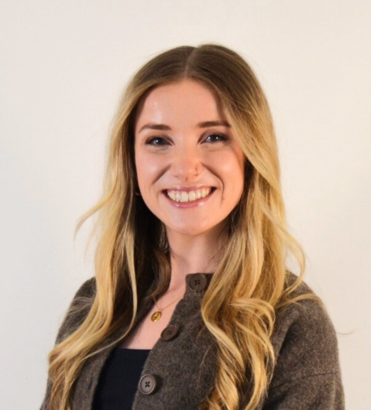 Eloise Garbutt has long blonde hair, she is smiling at the camera and wearing a smart brown cardigan